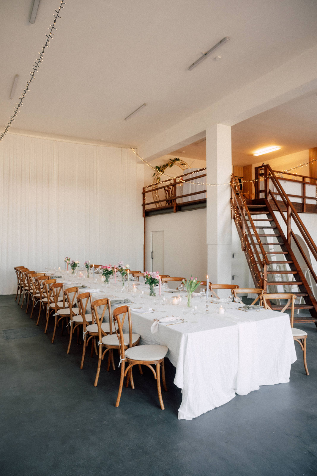 Lange festliche Tafel mit Holzstühlen und Lichterketten im Loft